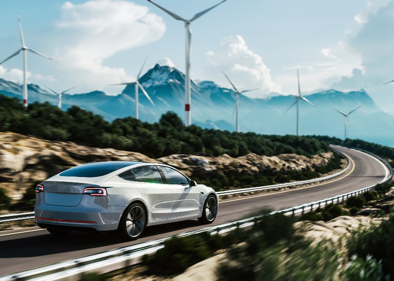Electric vehicle driving down winding road with wind turbines ahead